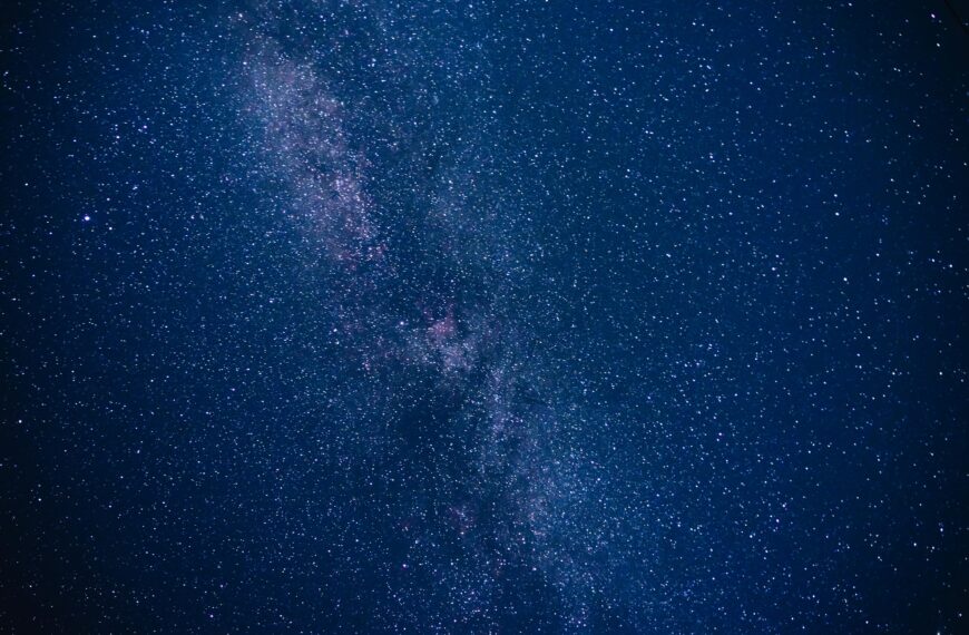 The Milky Way, a pale band of purple and white stars, across a dark blue sky.